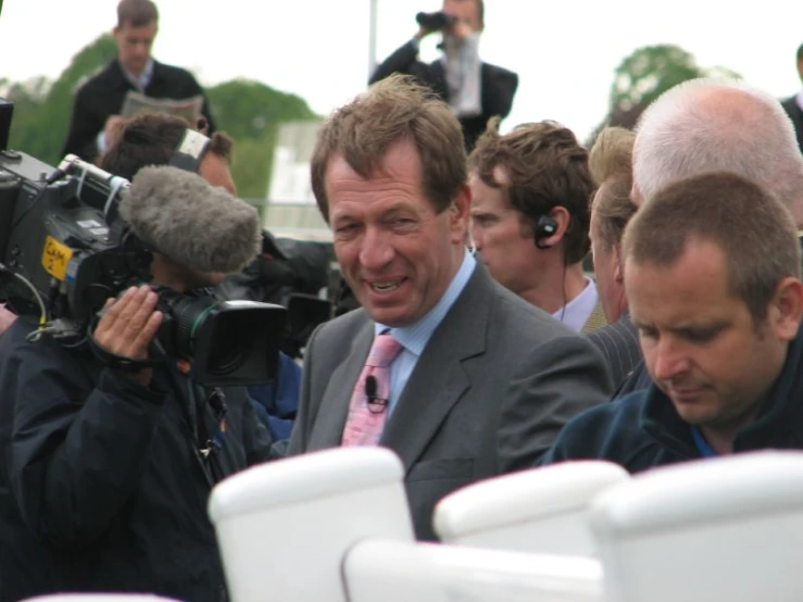 two men in suits talking and surrounded by reporters