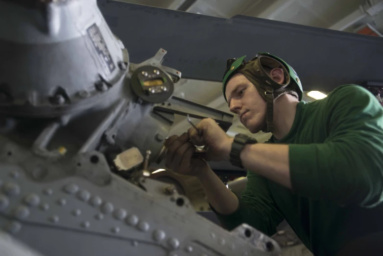 a man in green shirt and goggles working on metal thing