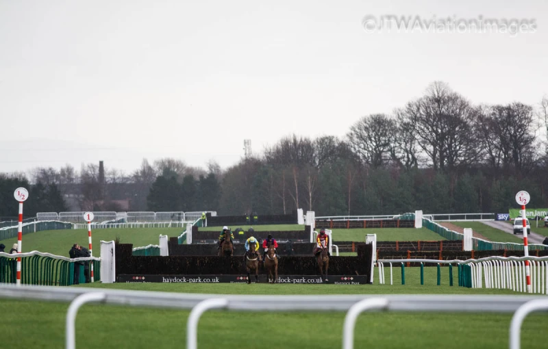 jockeys riding their horses over the fence at a horse race