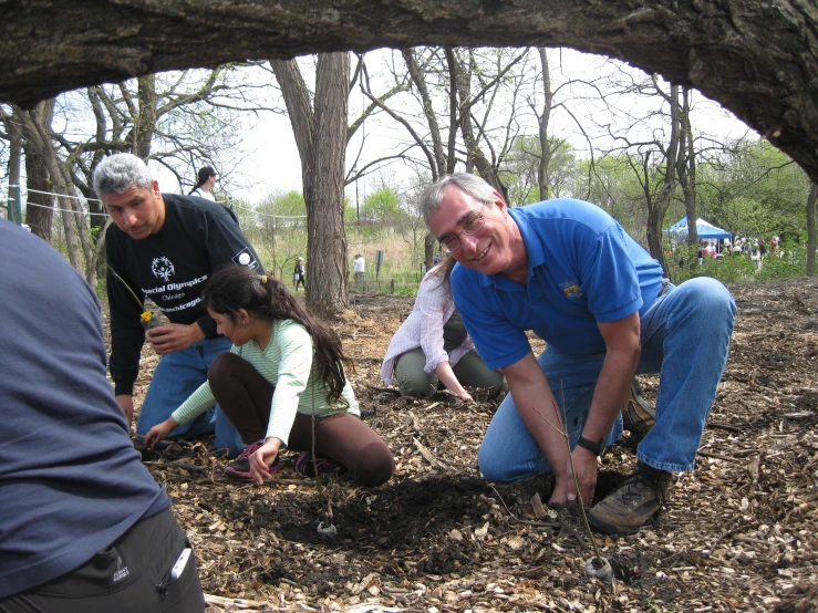 people are kneeling down in a pile of dirt with a tree