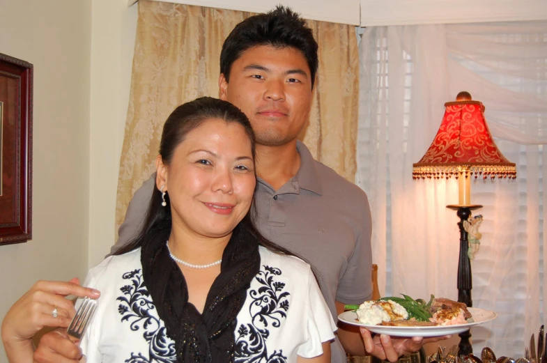 a man standing next to a woman holding up a plate with food