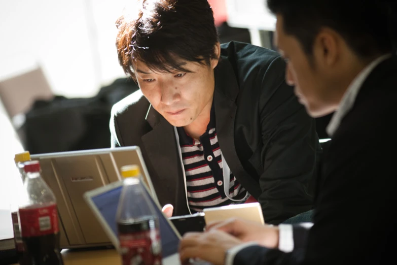 two men are looking at their phones and laptops