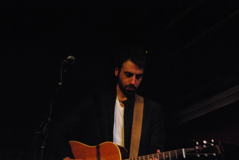 a man holding an acoustic guitar playing a song on a stage