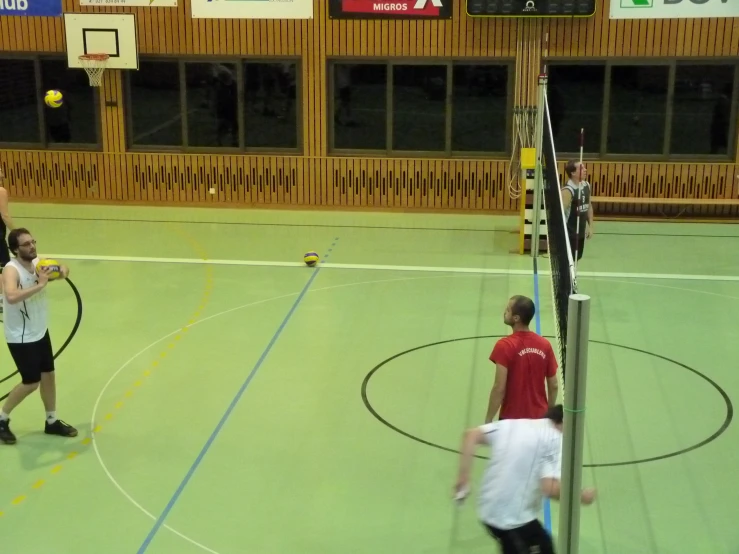 people are playing volleyball in a gymnasium with large windows