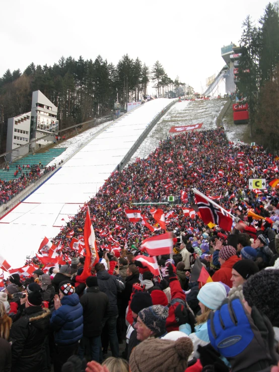 the crowd is standing at the bottom of a ski slope and waving their flag