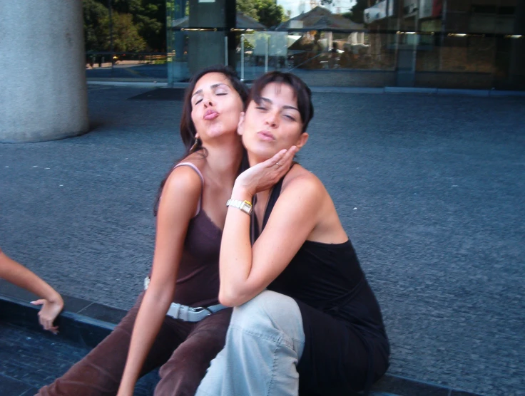 two women sitting down together on a sidewalk