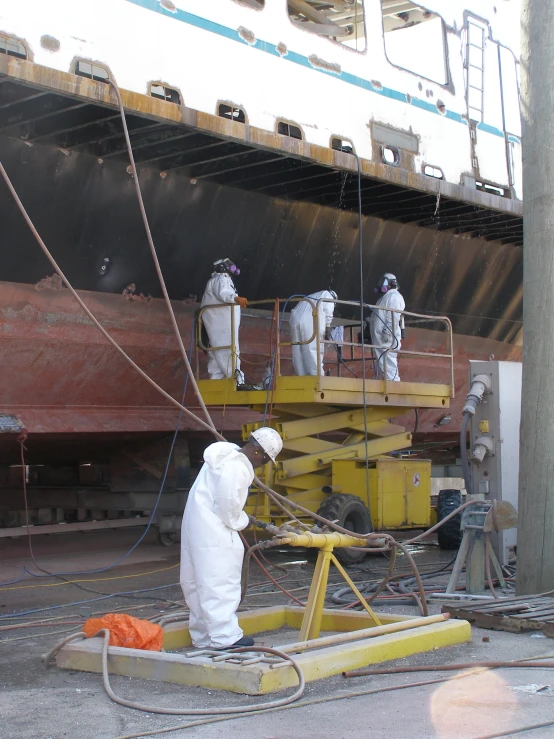 workers in protective gear on a deck work to remove rust from the ship