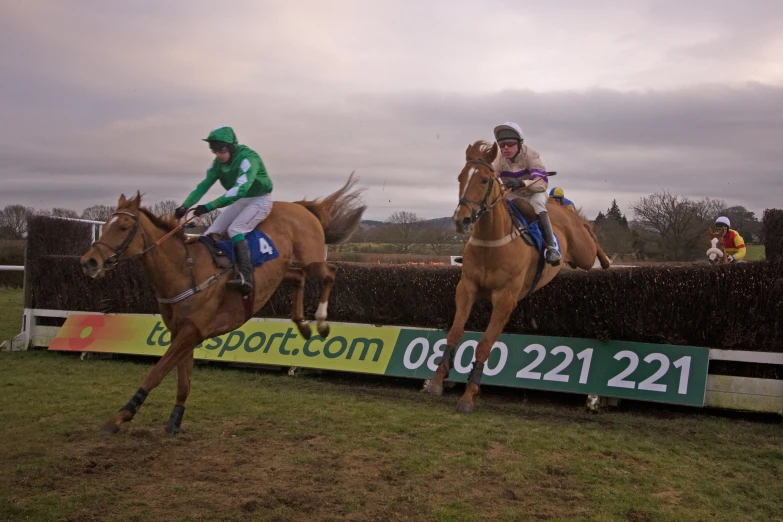 two men riding horses as they are jumping over an obstacle