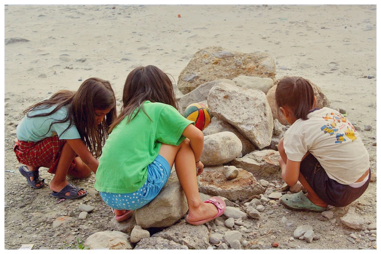 three children sitting on a rock playing with each other