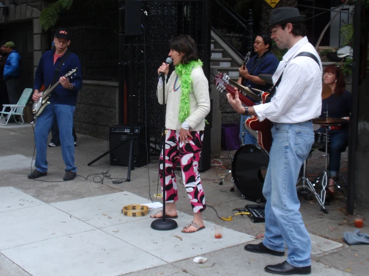 a woman wearing heels and a green scarf sings into a microphone as a musician stands in front of her