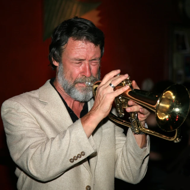 a man with a beard and a white suit on, holding his ss trumpet up to his face