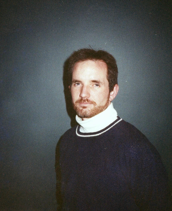 a man with a beard standing in front of a black wall