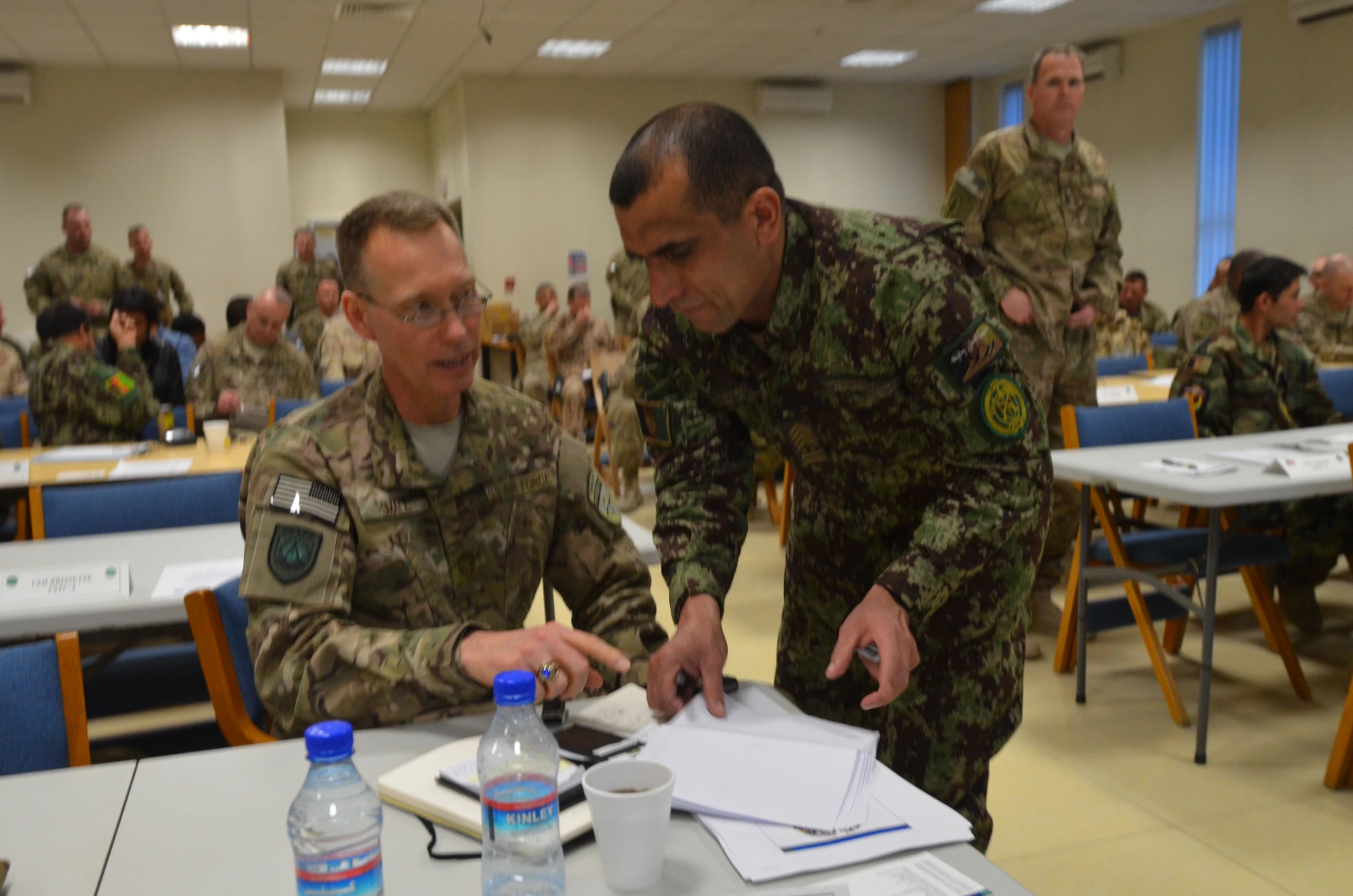 two military men in uniforms look at documents with water bottles