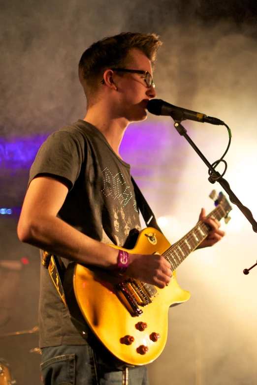 young man in grey shirt playing guitar in front of microphone