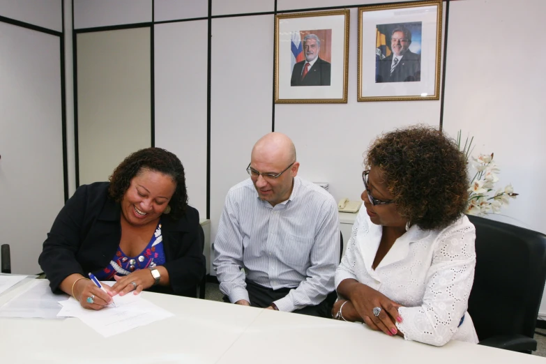 three people sitting at a desk smiling and discussing soing