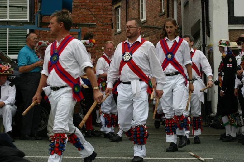 men dressed in white and red parade uniform carry flags through town