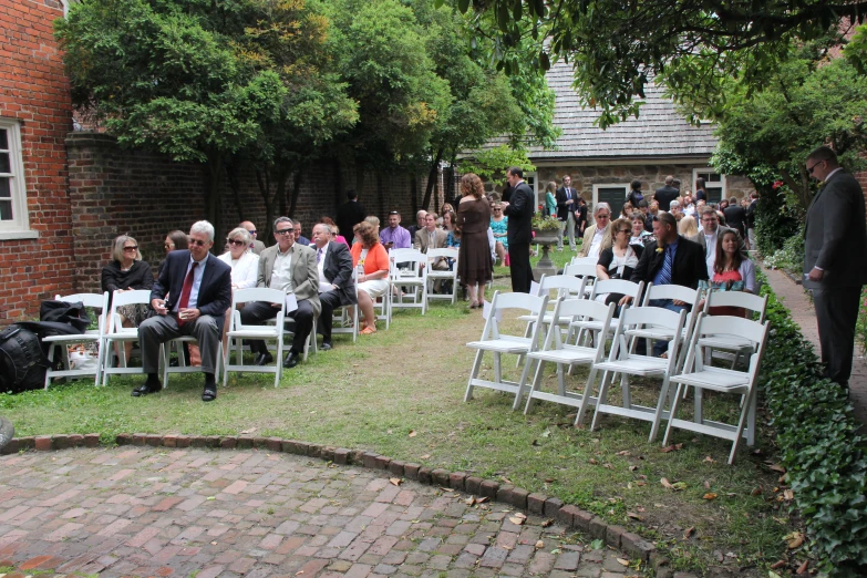 people sitting in chairs on the grass during a wedding ceremony
