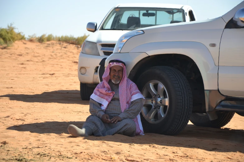 a man in a hijab sits next to two trucks