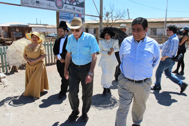 a group of men and women wearing western clothes, one man in a hat and the other a man in a white shirt and tan pants