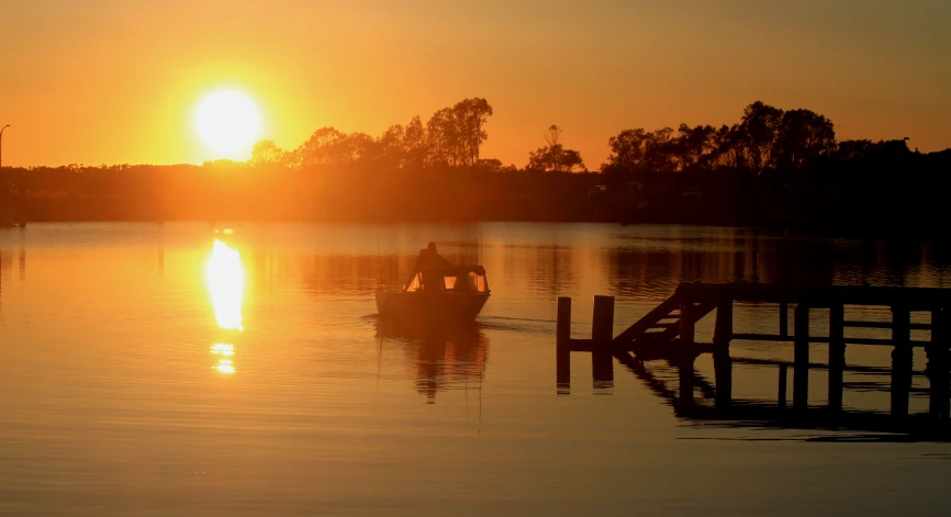 a boat floating along a river with the sun setting in the distance