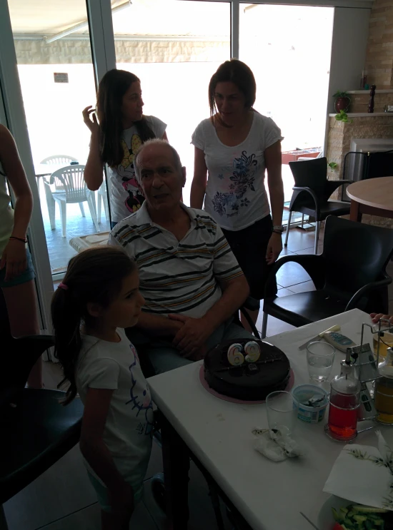 the woman is sitting behind the child at the table with her birthday cake