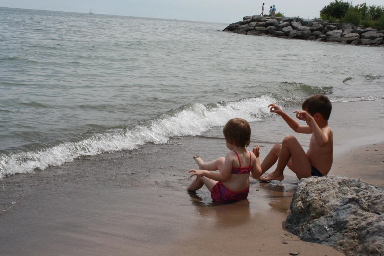 two little boys sitting on the beach and playing with water