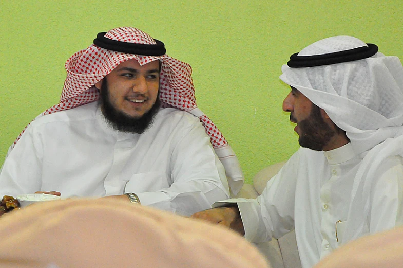 two men sitting down talking while wearing head coverings