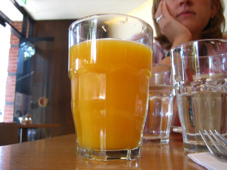 a glass filled with orange juice and a woman sitting down behind it