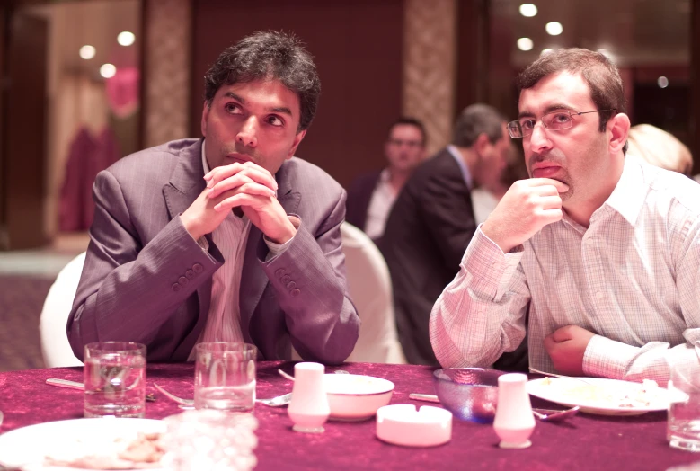 two men sitting at a table looking off to the side