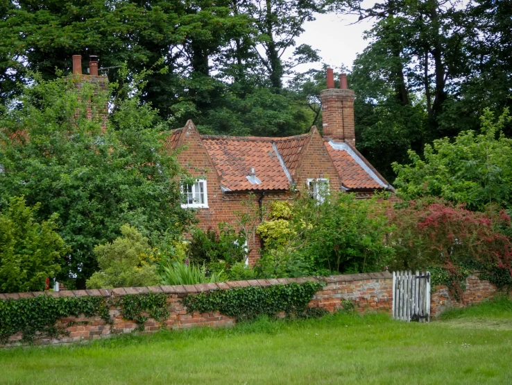 a house behind a wall that is surrounded by trees and shrubs