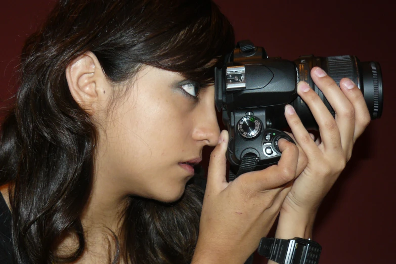 a girl holding a camera up to the side with both hands