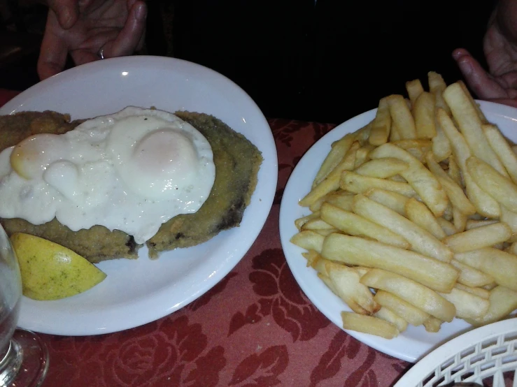 two plates of food with meat, fries and gravy are sitting next to each other