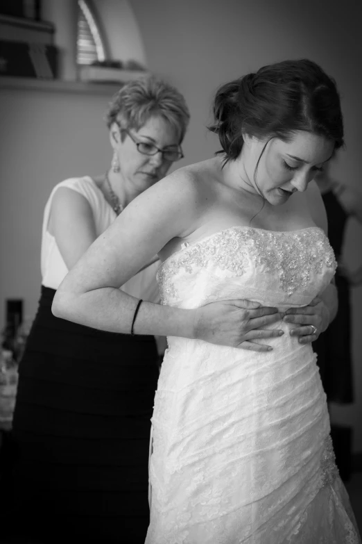 a woman in a dress helping another woman get dressed