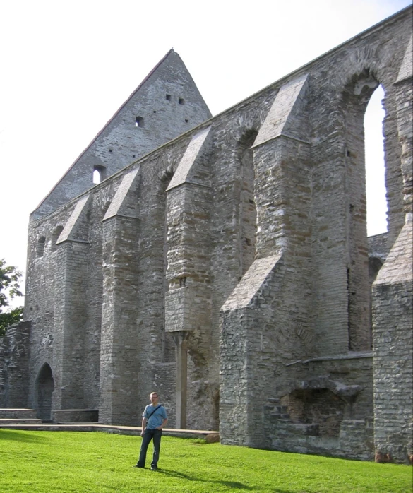 a man stands in the green grass beside an old brick building