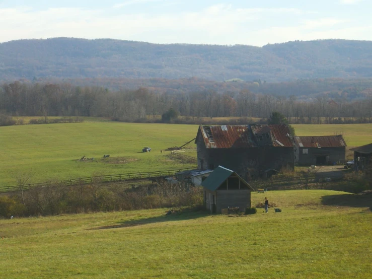 an old barn sits in a green field, with mountains behind it