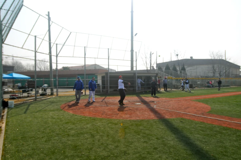 people playing baseball on a green field with an empty cage