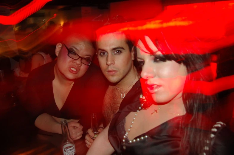 three people pose in a dark bar with one looking at the camera