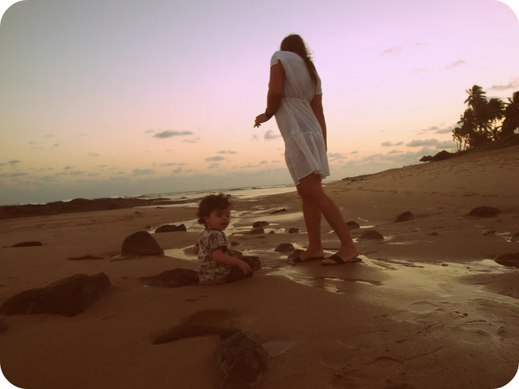 a woman and small child on the beach playing with rocks