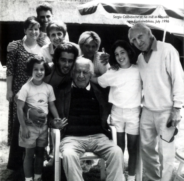 an older man in a wheelchair surrounded by people