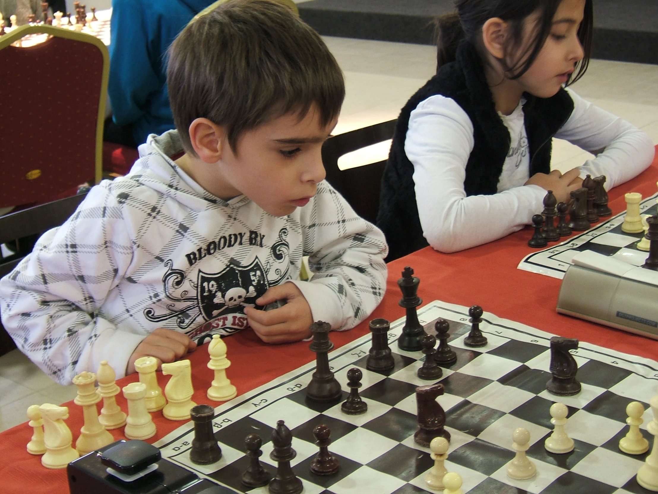 two children playing chess at a table with red cloth