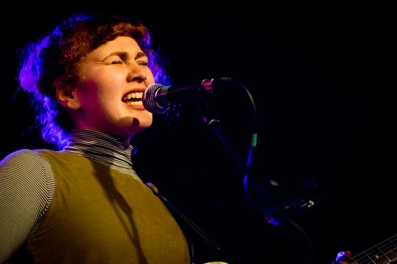 a woman playing guitar and singing into the microphone