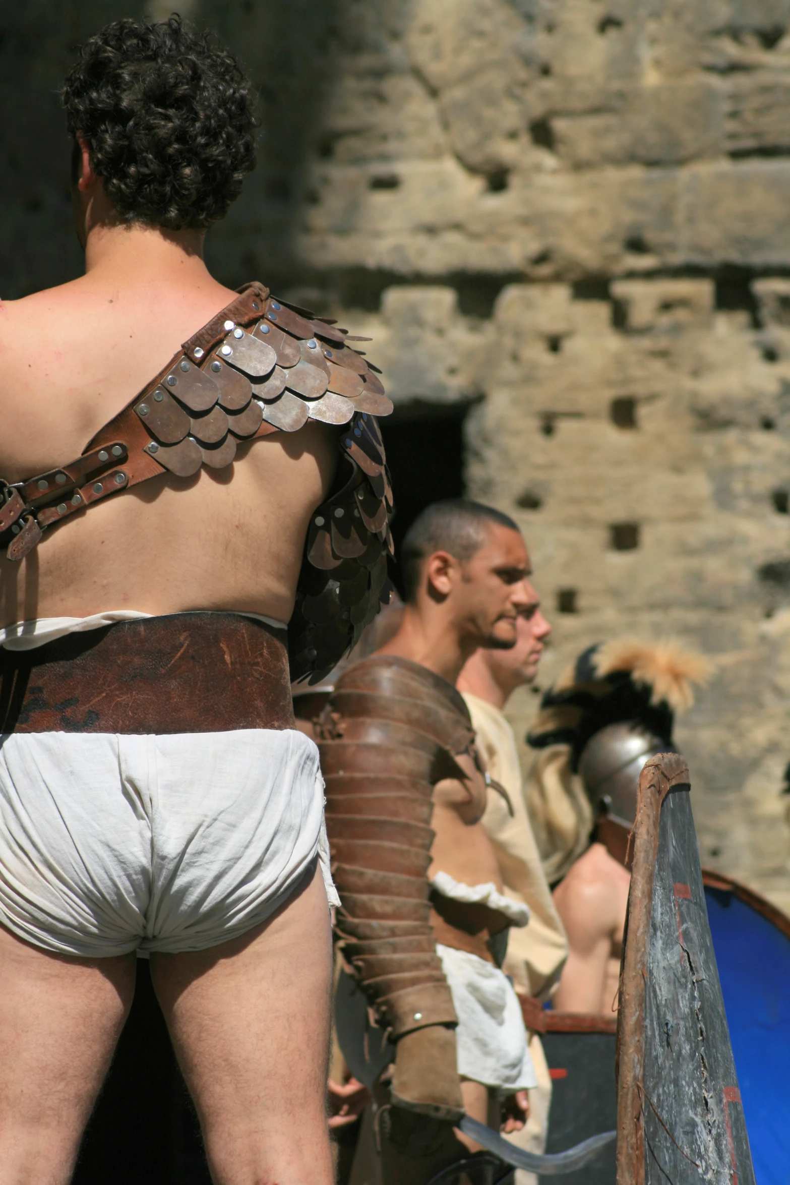 two men in roman costumes with a stone wall behind them