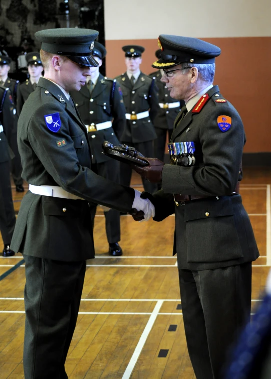two uniformed men shaking hands while another man in uniform is next to him