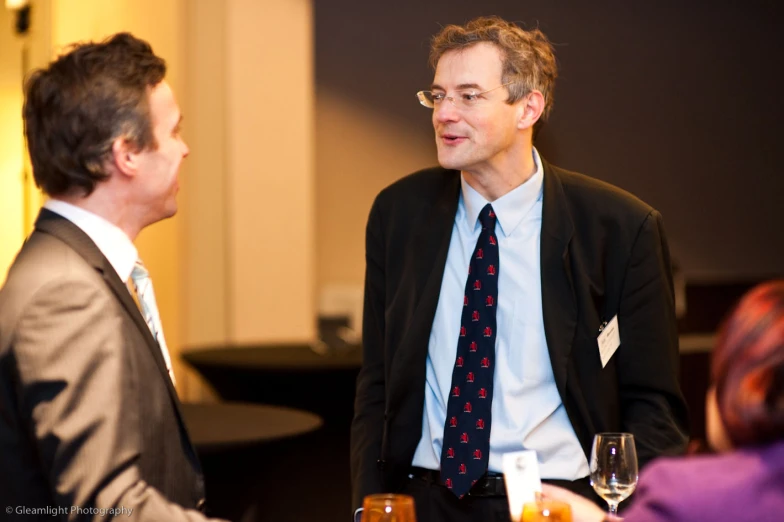 two people dressed in suits talking and having drinks