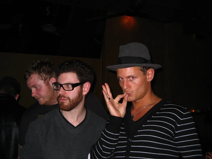 three men dressed in black and white, one smoking and the other smoking a cigarette