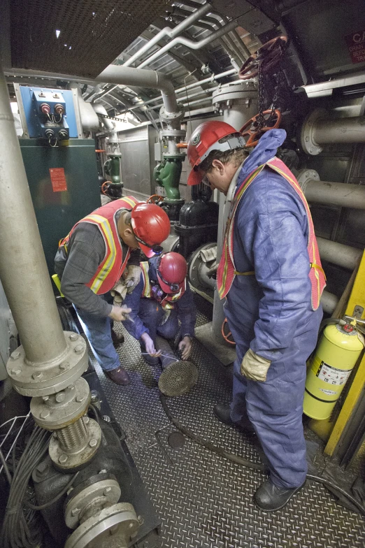 two men standing in front of pipes working on a machine