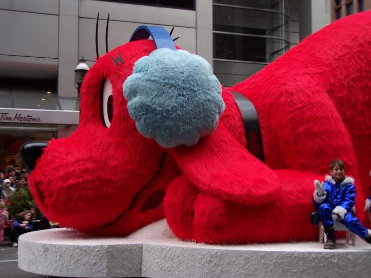 two giant stuffed animals with small children sit on cement blocks in front of a building