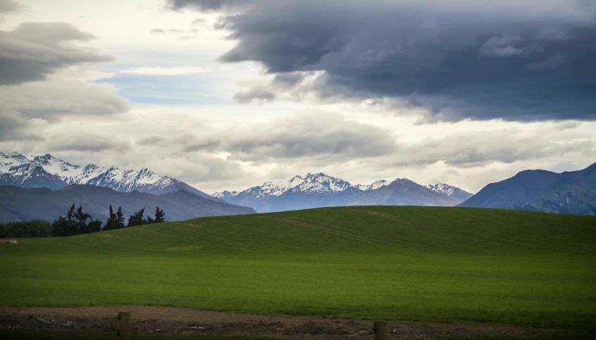 green hillside with dark clouds and mountains