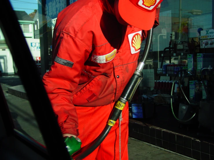 a man wearing red is pumping a gas nozzle