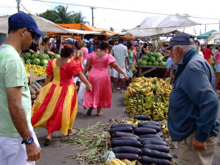 a man and woman walking past several vendor tables with produce